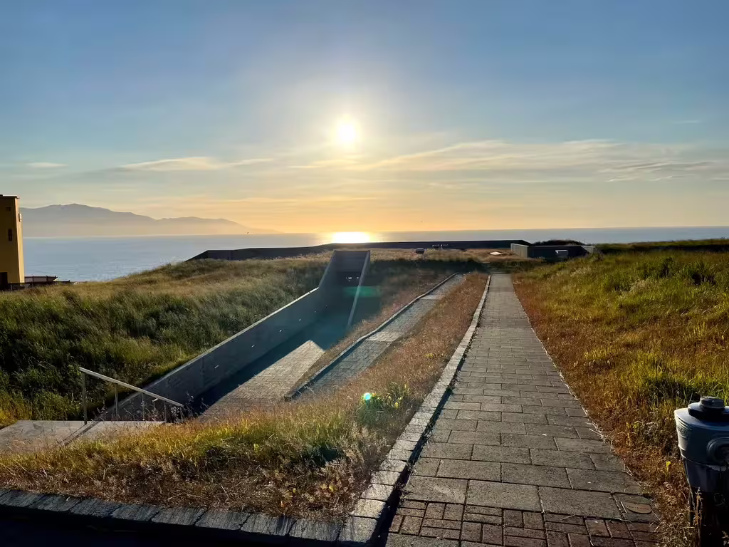 Sunset over ocean viewed from grass-covered rooftop with stone walkway in Akureyri, Iceland