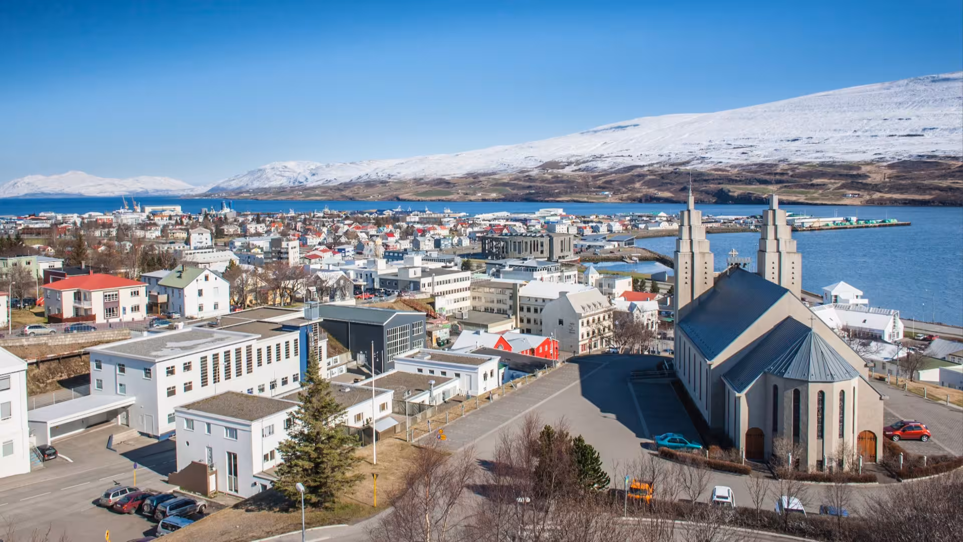 Aerial view of Akureyri town with church, colorful buildings, harbor, and snow-capped mountains in Iceland