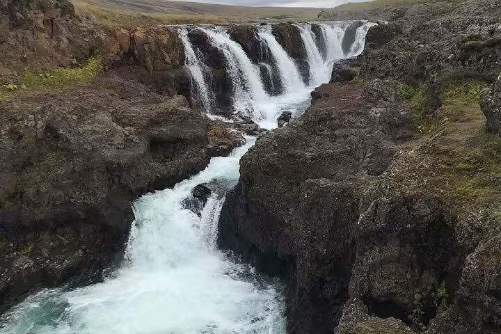 Multi-tiered waterfall cascading through rocky canyon near Akureyri, Iceland