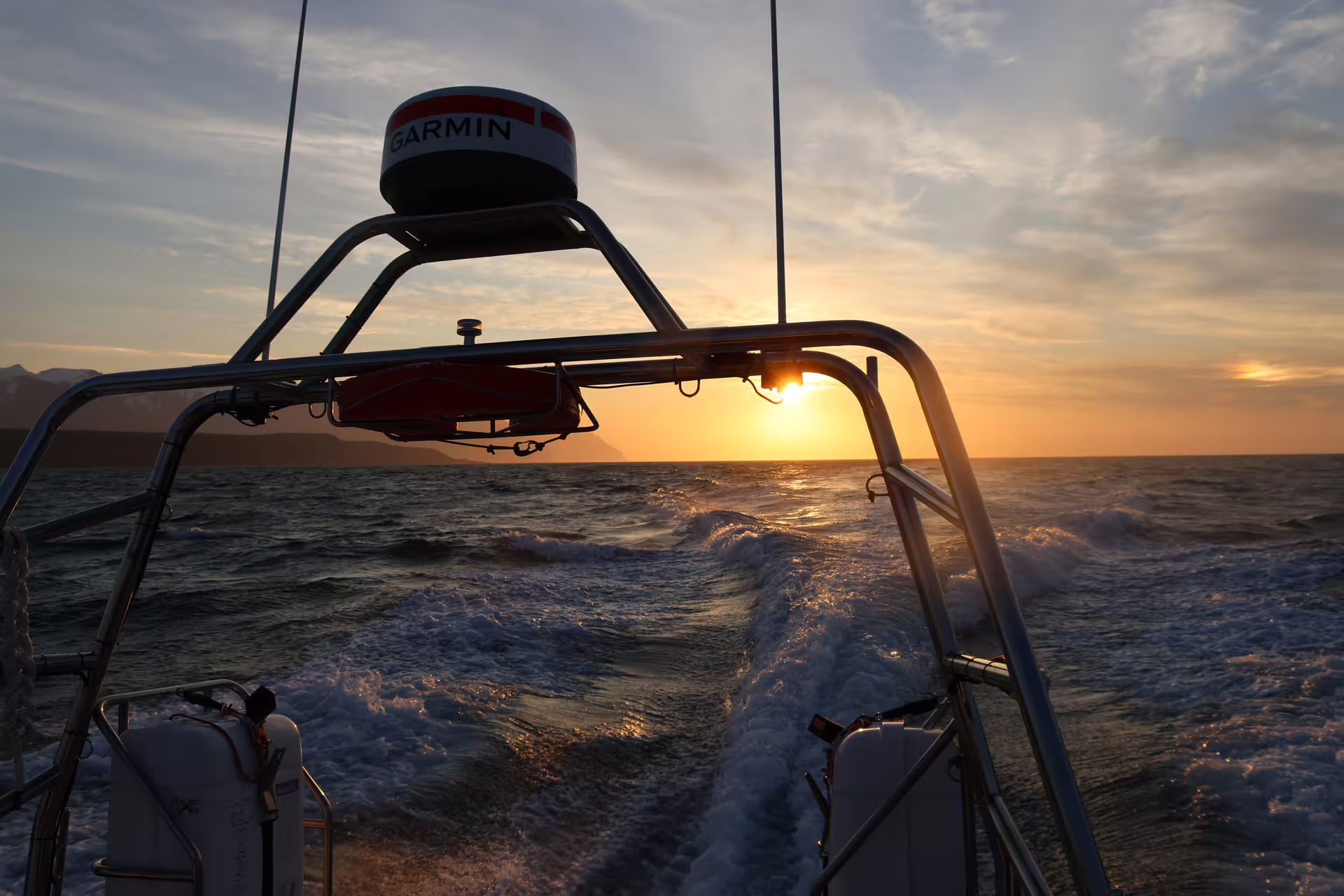 View from stern of whale watching boat with Garmin radar, ocean wake, and golden midnight sun on horizon