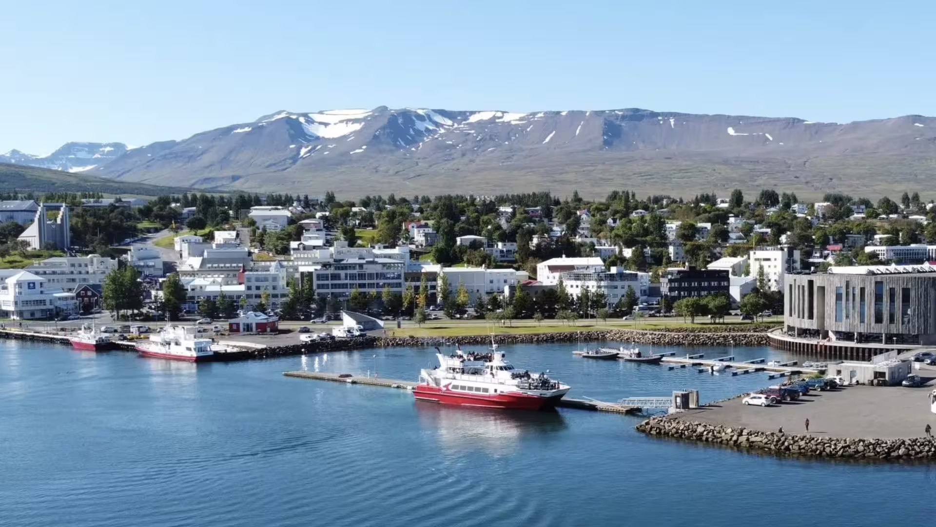 Akureyri harbor with red whale watching boats docked in Eyjafjordur Fjord, snow-capped mountains behind