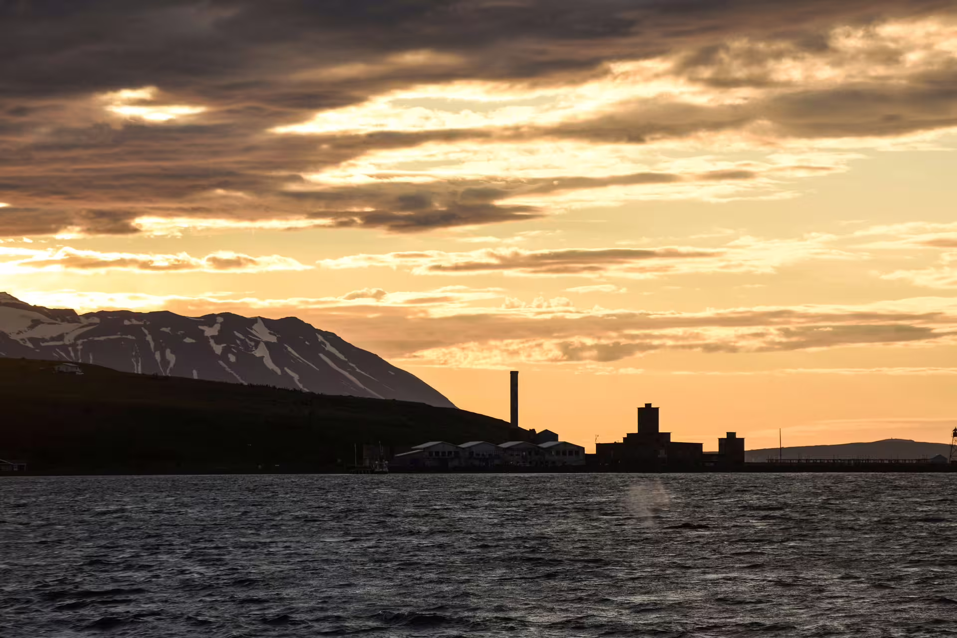 Akureyri harbor silhouette at midnight sun with snow-capped mountains and golden sky over calm fjord waters