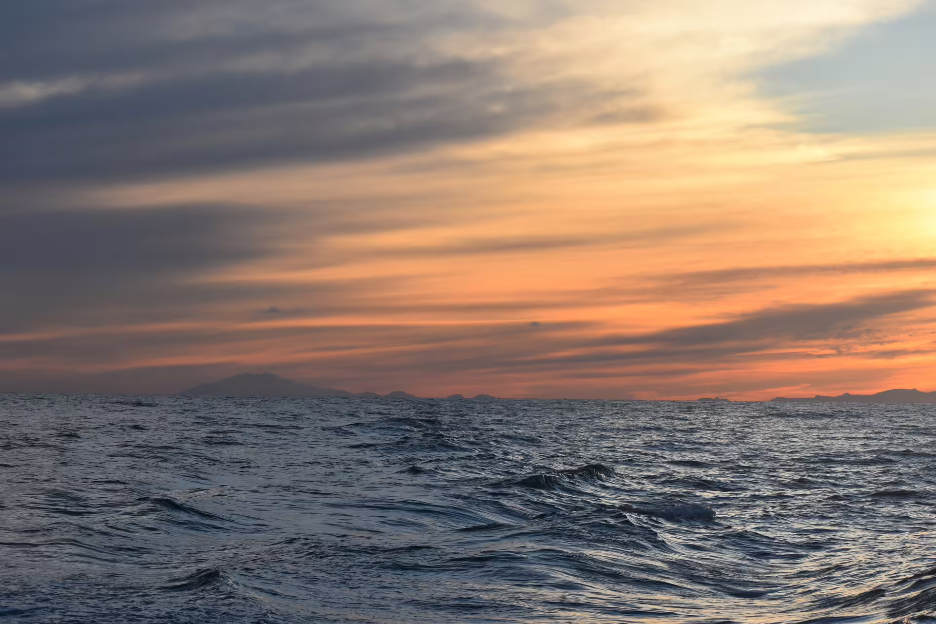 Choppy ocean waves at sunset with mountain silhouettes on the horizon during midnight sun in Akureyri