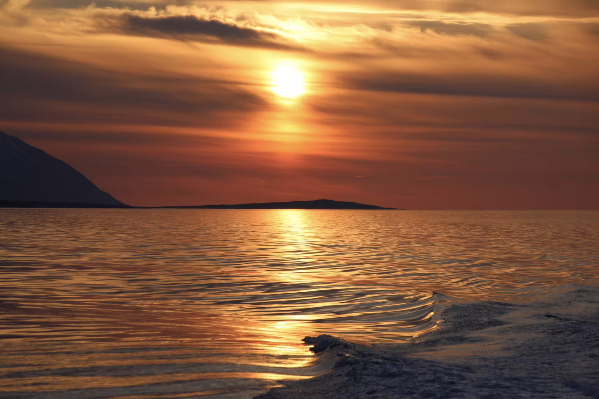 Golden midnight sun glowing over calm ocean waters with silhouetted mountain islands near Akureyri, Iceland