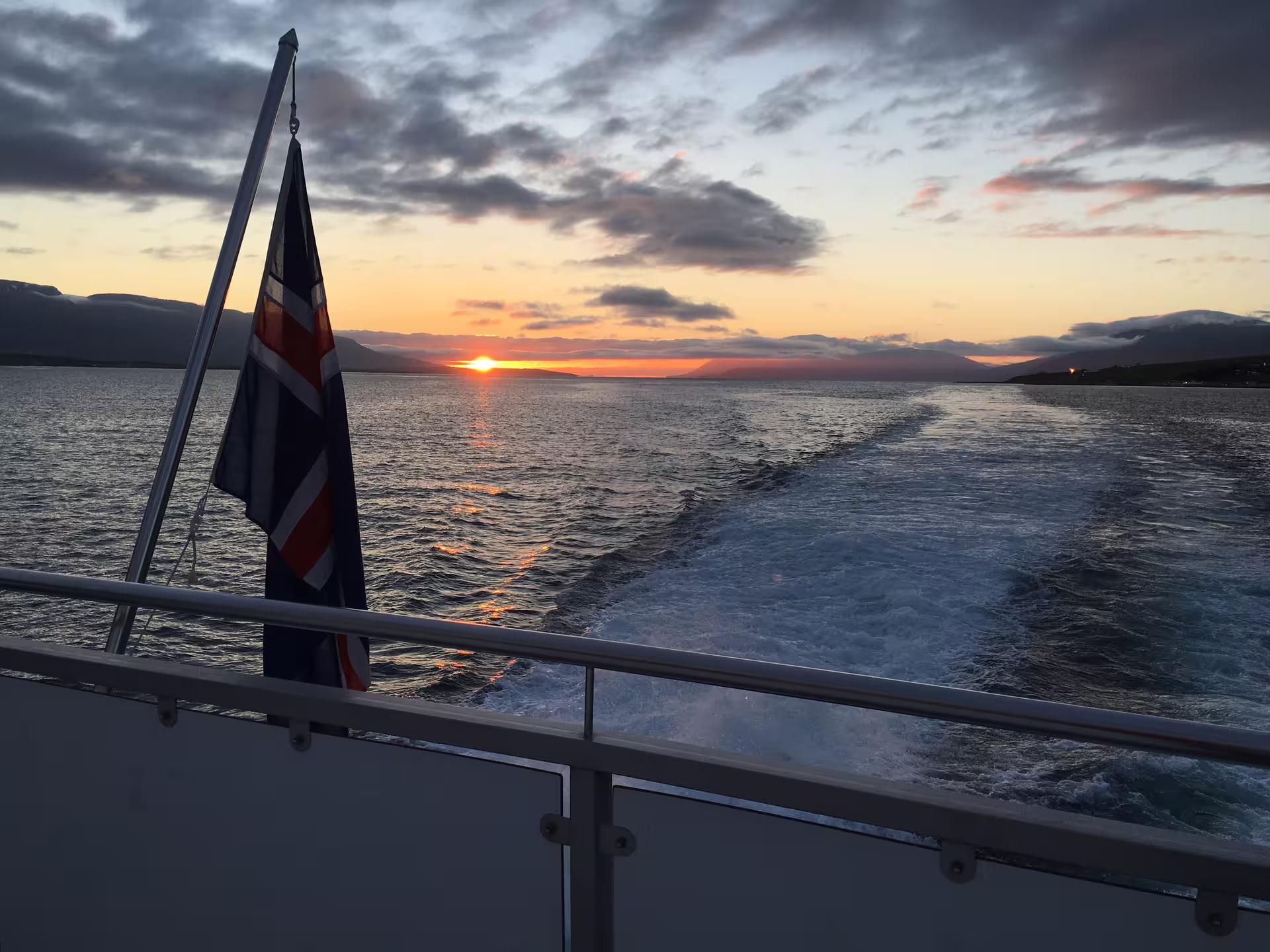 View from stern of whale watching boat in Akureyri with midnight sun sunset over calm fjord waters