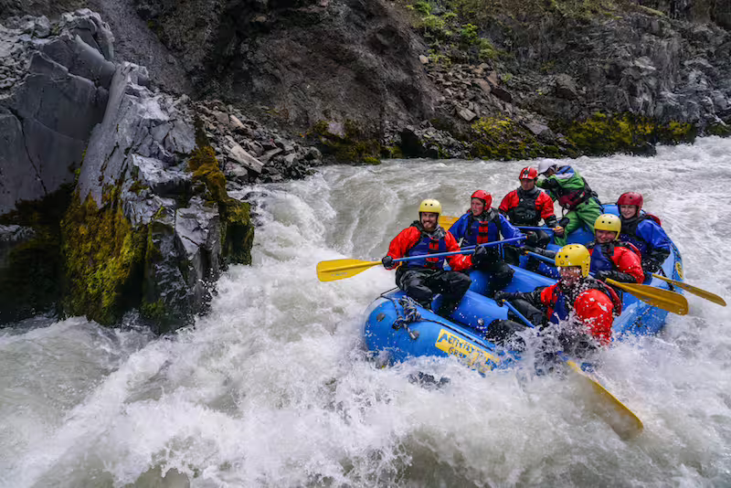 Group of rafters navigating white water rapids in a blue raft through a rocky canyon in Akureyri