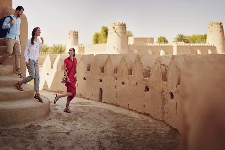 Tourists exploring Al Ain's historic architecture, walking along ancient fortress walls on a private city tour.