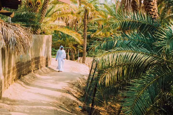 Man in traditional attire walking through lush palm-lined path in Al Ain's private garden tour.