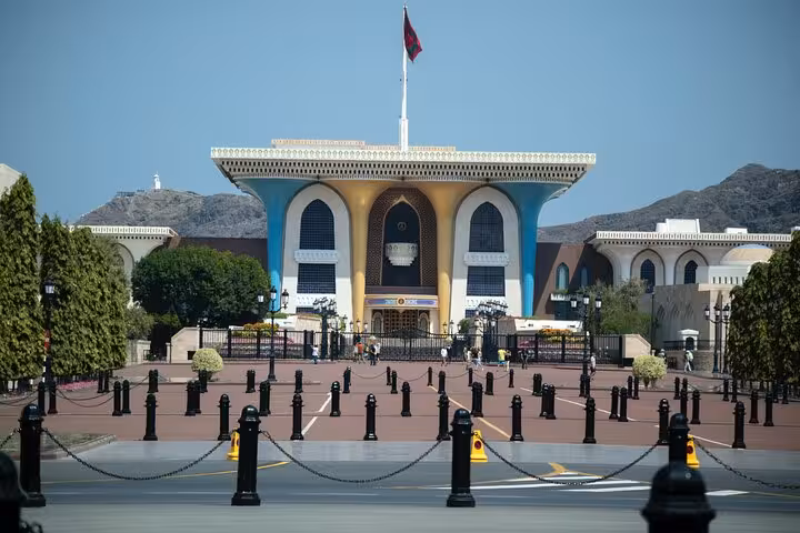 Colorful Al Alam Palace in Old Muscat with Omani flag and mountains, a highlight stop on Muscat evening sightseeing taxi tours