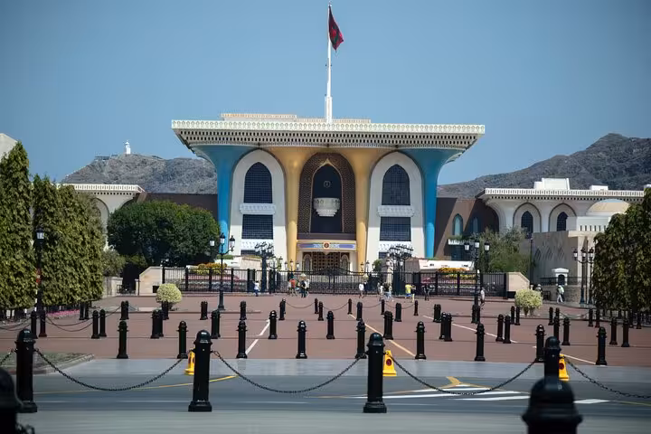 View of Al Alam Palace in Muscat with Omani flag, colorful façade and mountain backdrop on a private sightseeing tour