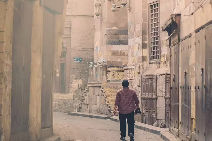 Traveler strolling Al-Mu'izz Street in Islamic Cairo, historic stone facades on guided tour with dinner