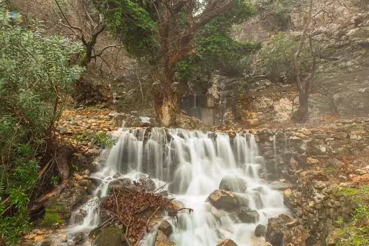 Small cascading waterfall over mossy rocks in forested gorge on Ikaria Hike: Alama Spring, tranquil nature escape