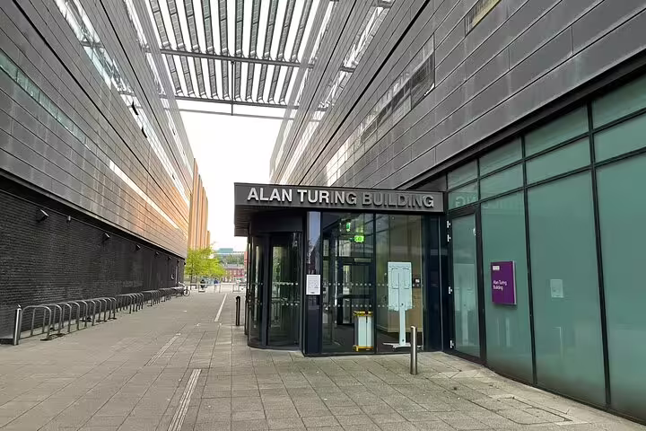 Entrance to the Alan Turing Building in Manchester, a modern dark-clad building with glass doors