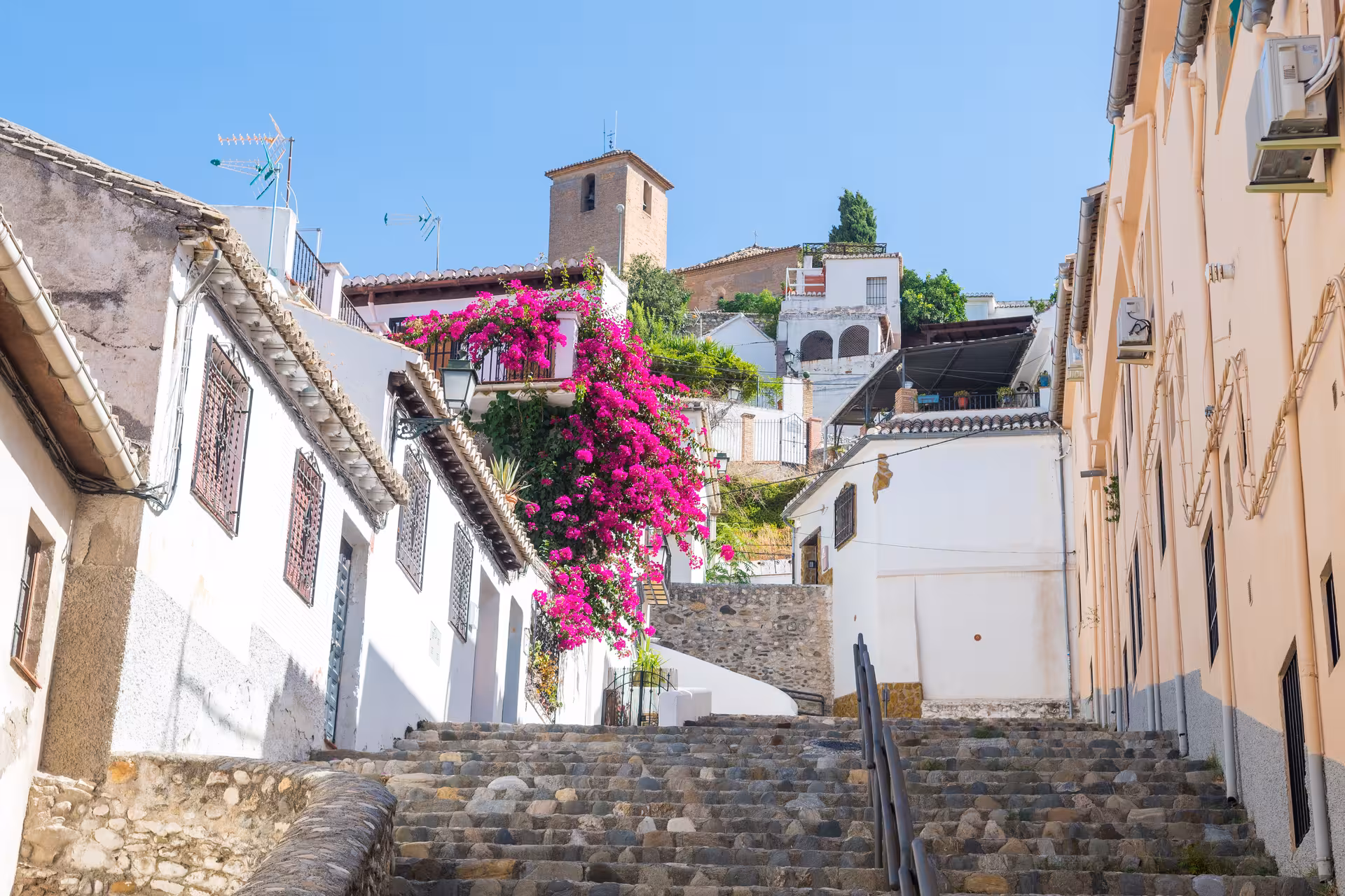 Charming cobblestone street in Albaicín with vibrant bougainvillea and historic architecture under a clear blue sky.
