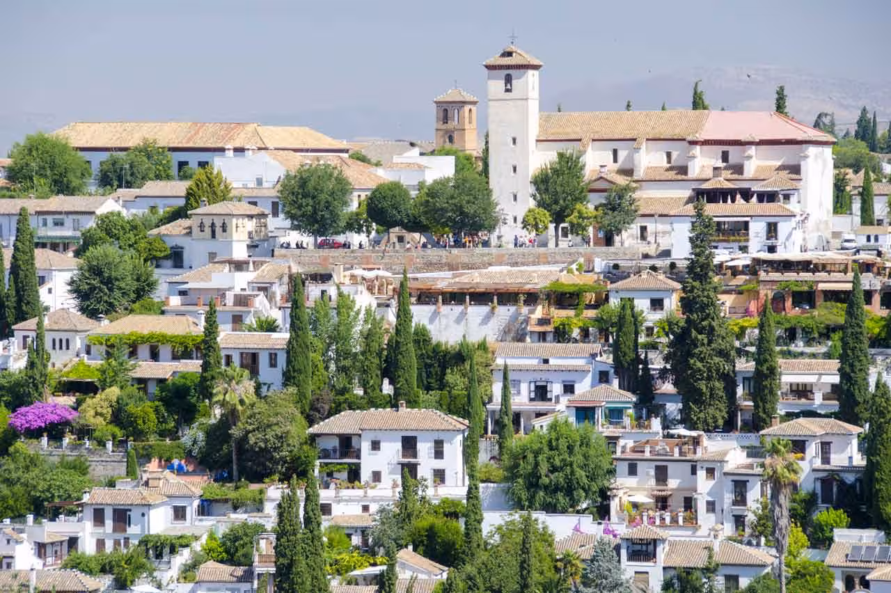 Panoramic view of the picturesque Albaicín neighborhood with whitewashed houses and lush gardens under a clear sky.