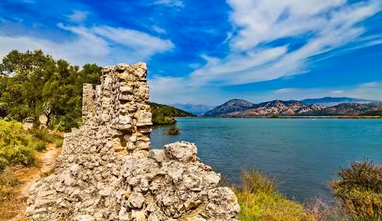 Scenic ruins by the serene Butrint Lake with mountainous backdrop in Albania, ideal for cultural and nature exploration.