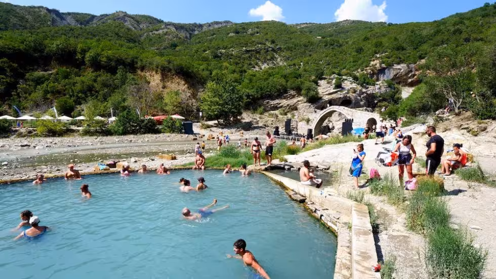Tourists enjoying Albanian hot springs with scenic views and historic bridge, perfect for adventure and relaxation.