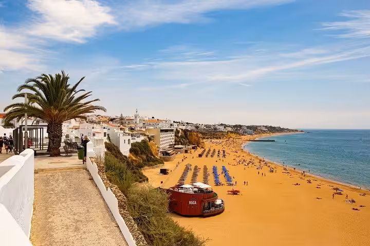 Panoramic view of Albufeira's golden beach with lined parasols and the blue Atlantic Ocean under a clear sky.