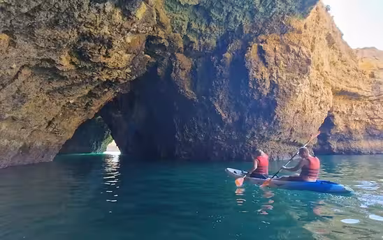 A couple kayaking toward a stunning Albufeira sea cave arch on turquoise waters during a private full experience tour