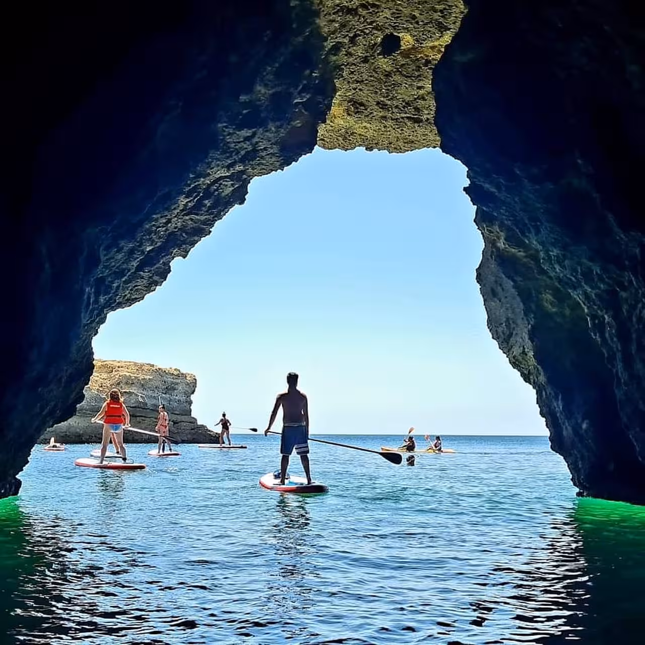 Paddleboarders exploring dramatic Albufeira sea cave arch on a private SUP tour in clear blue waters