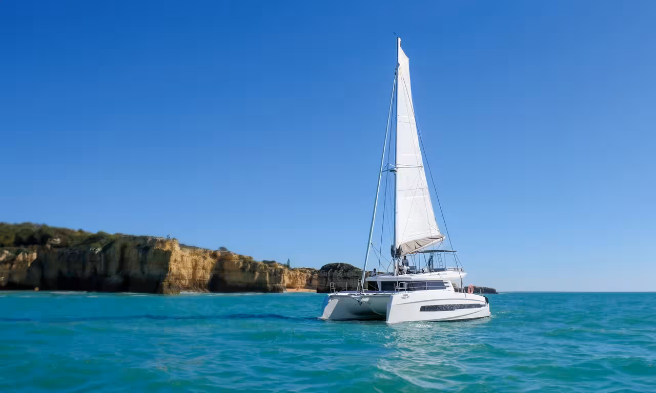 White catamaran sailing on turquoise waters near Albufeira golden cliffs on a private Algarve sunset cruise