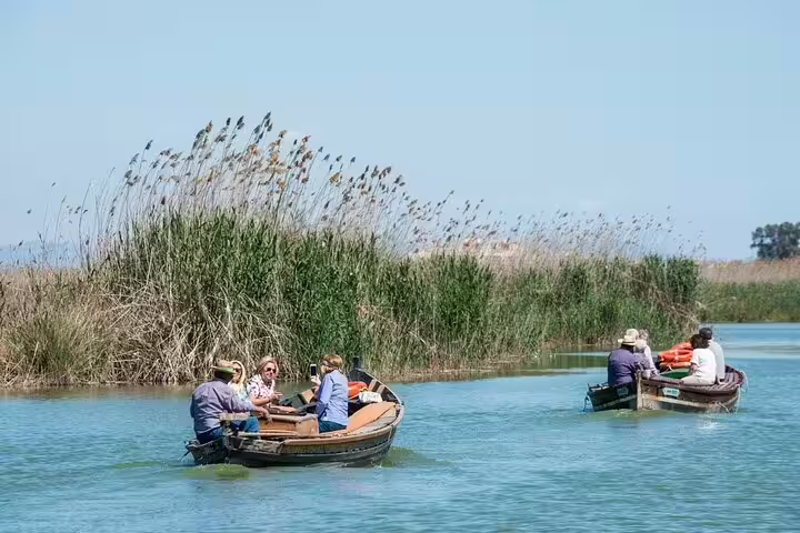 Visitors enjoy a serene boat ride through Albufera's lush waterways, part of a private day trip with paella and nature trek.