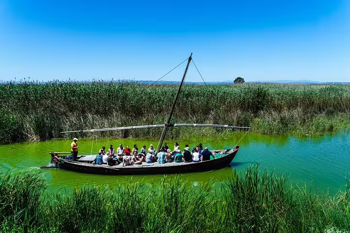 Tourists enjoy a scenic boat ride through Albufera's lush wetlands on a private day trip featuring paella and nature trekking.