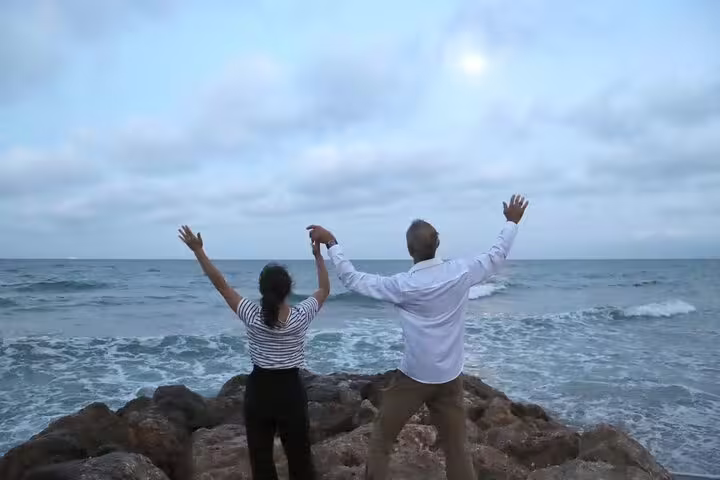Couple enjoying scenic ocean view on a rocky shore during a private Albufera day trip with paella, boat ride, and nature trek.