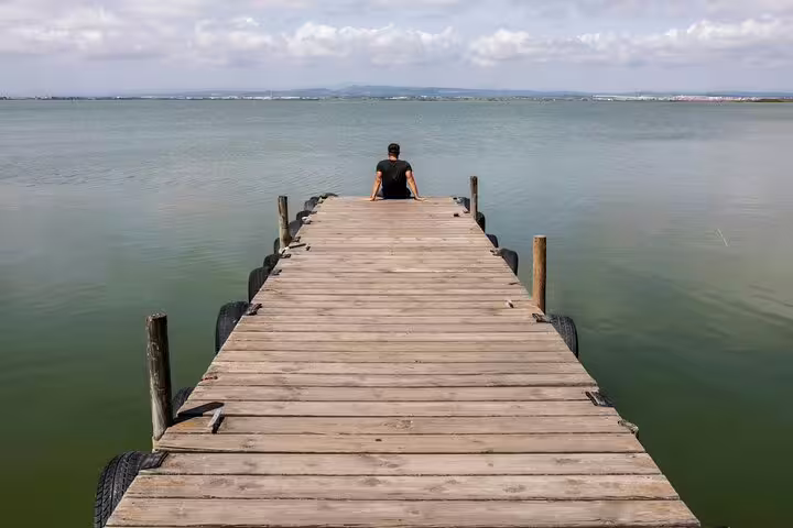 A person sits at the end of a wooden pier overlooking Albufera Lagoon, highlighting serene nature and relaxation on a private day trip.