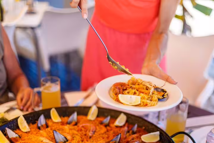 Person serving seafood paella with lemon wedges during a Private Albufera Day Trip, showcasing authentic Spanish cuisine.