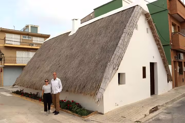 Couple stands outside traditional thatched-roof house in Albufera, perfect for a private day trip with paella, boat ride, and nature trek.