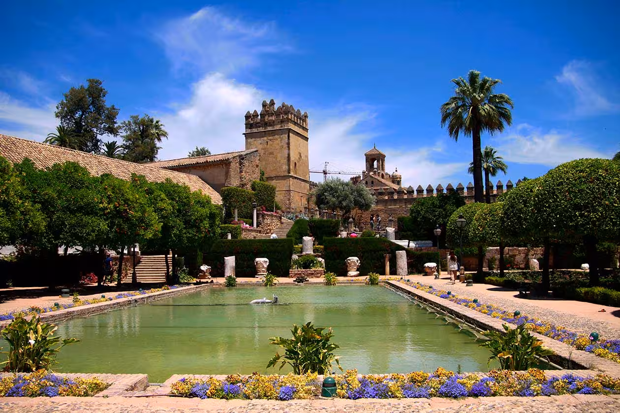 Elegant courtyard with a central pond and historic towers at the Alcázar of the Christian Monarchs in Córdoba.