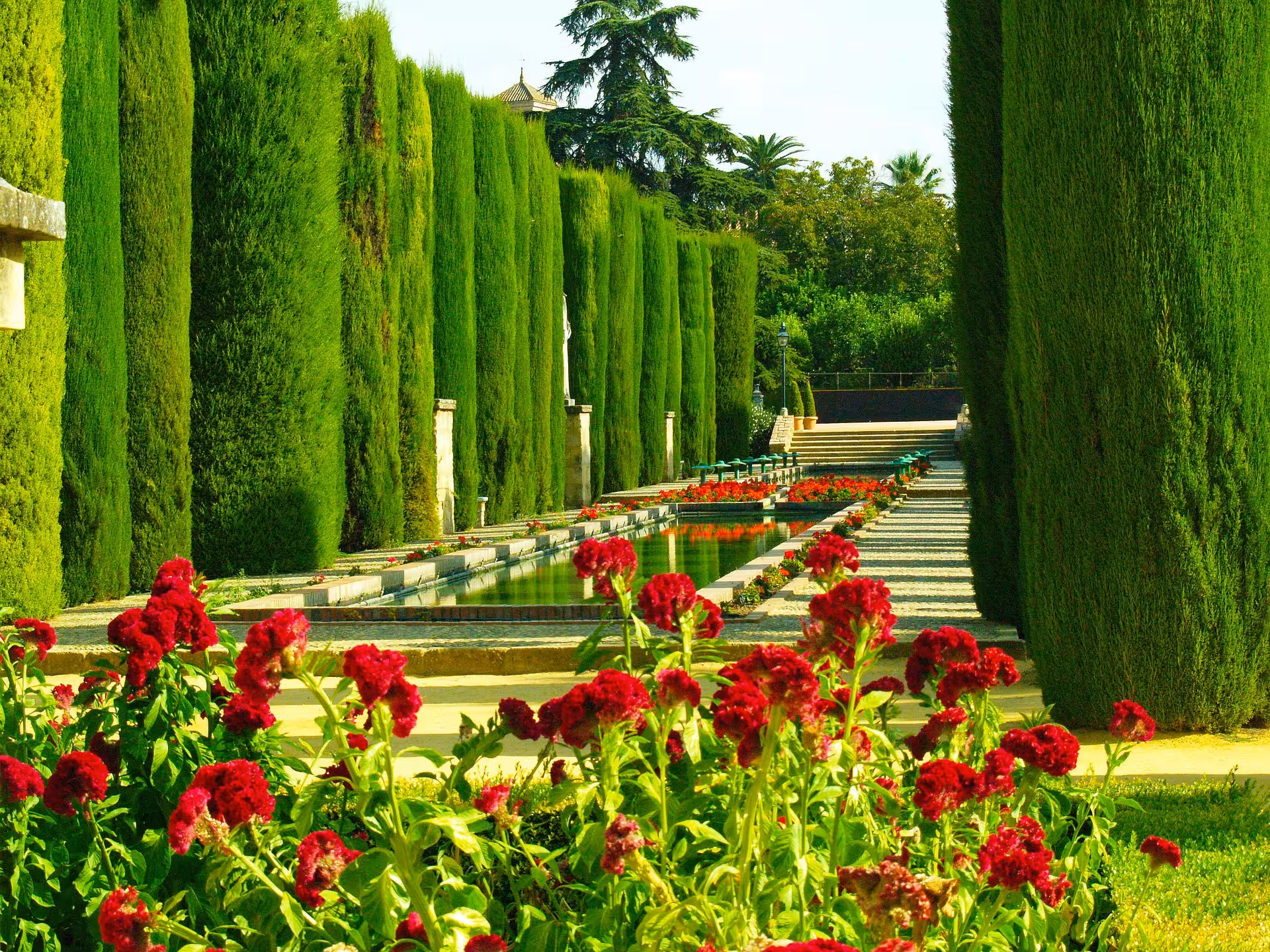 Lush gardens with vibrant red flowers and a serene waterway at the Alcázar of the Christian Monarchs in Córdoba.