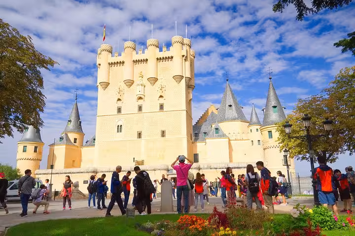 Tourists explore the enchanting Alcázar of Segovia with its fairy-tale turrets and vibrant gardens on a sunny day tour.