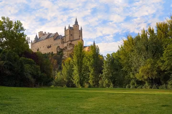 The majestic Alcázar of Segovia rises above lush greenery, a must-see on full-day excursions from Madrid.