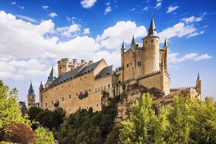 The majestic Alcázar of Segovia, with its fairy-tale spires, stands prominently under a vibrant blue sky on the Madrid day tour.
