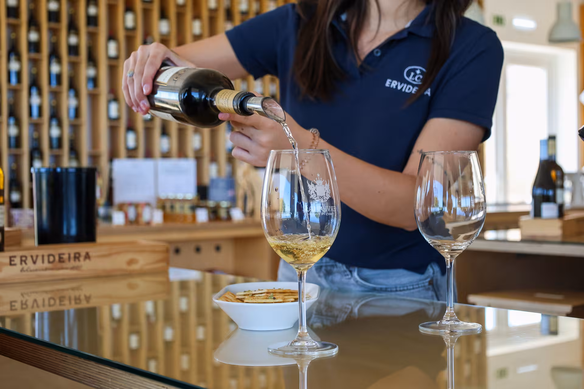 Wine tasting in Alentejo with a woman pouring white wine into glasses at a vineyard tasting room.