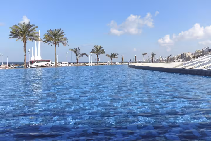 Reflective blue waterfront pool along Alexandria corniche with palm trees and Mediterranean sea views
