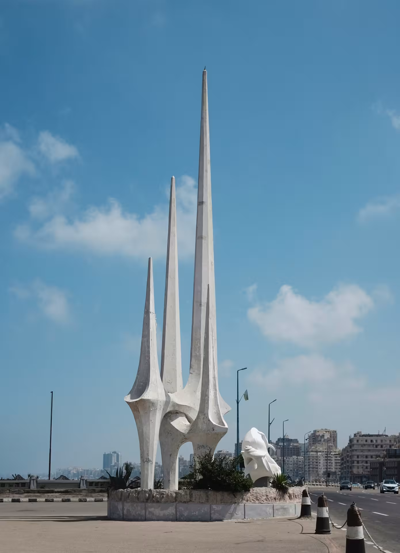 White modernist sculpture with three tall spires on Alexandria corniche waterfront road