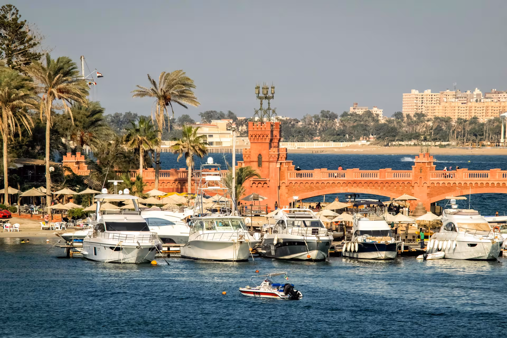 Marina with luxury yachts docked near a red brick arched bridge in Alexandria, Egypt