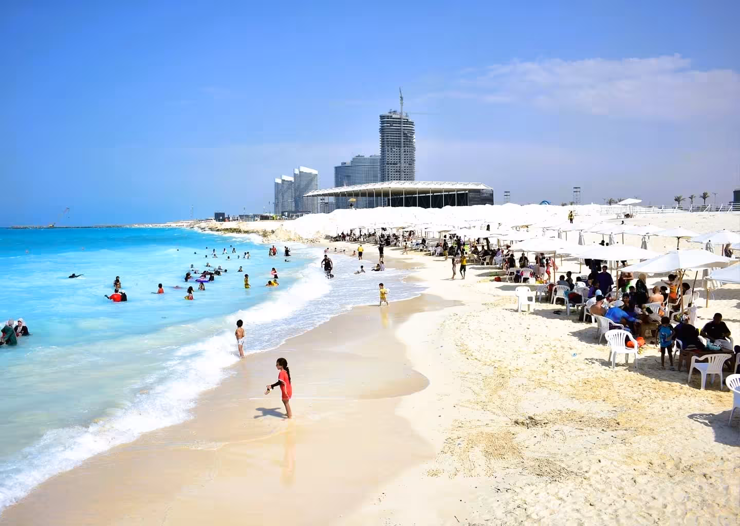 Sunny Mediterranean beach near Alexandria with white umbrellas, turquoise water, and modern city skyline