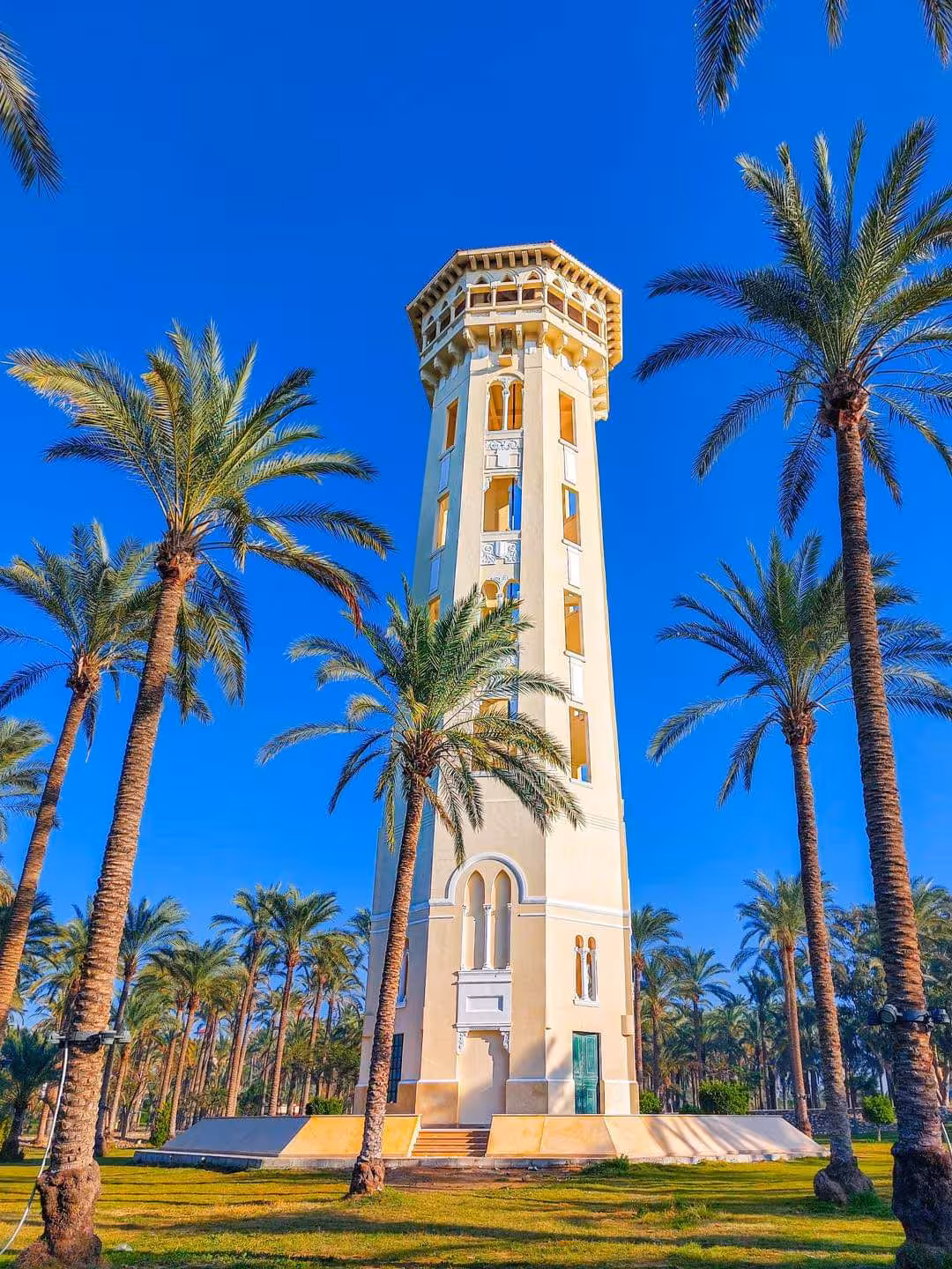 Ornate octagonal tower surrounded by tall palm trees in Alexandria's Royal Gardens under a clear blue sky