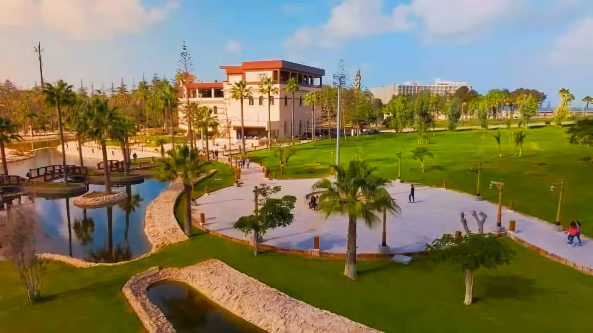 Aerial view of Alexandria Royal Gardens with palm trees, pond, walking paths, and historic building