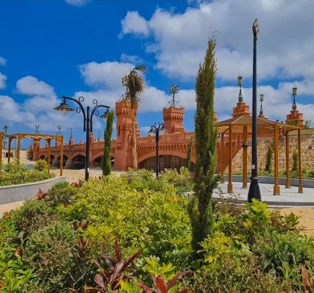 Red terracotta bridge with Moorish towers beside lush royal gardens in Alexandria, Egypt
