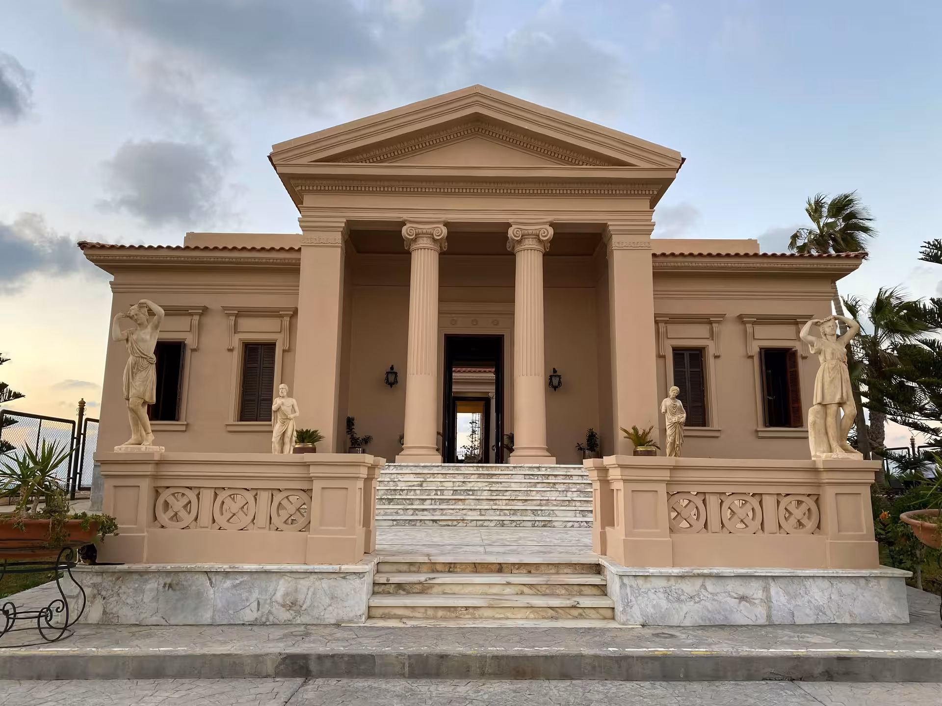 Neoclassical Alexandria Royal Palace facade with Ionic columns, marble statues, and grand staircase