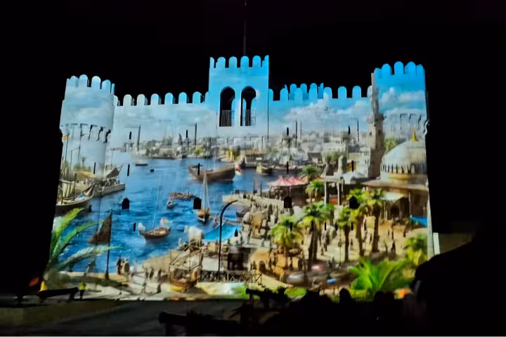 Alexandria sound and light show projection on ancient fortress walls depicting historic harbor scene with boats and palm trees