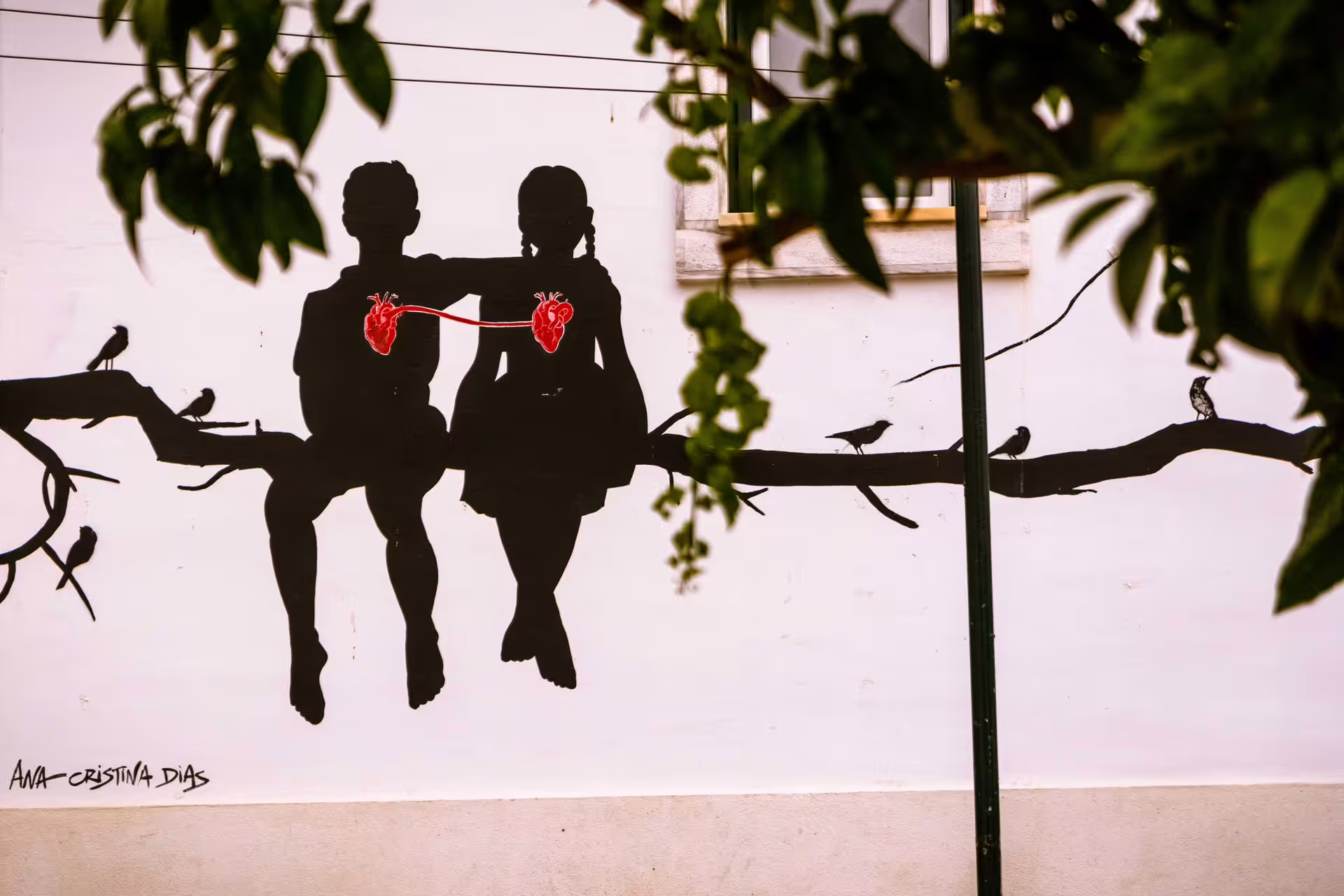 Street art mural in Alfama, Lisbon depicting two silhouettes with connected hearts on a branch, captured during a local photo walk.