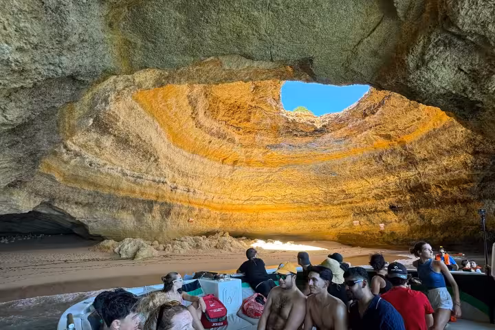 Group on a guided Algarve boat tour relaxes inside Benagil sea cave, watching waves and golden rock formations overhead