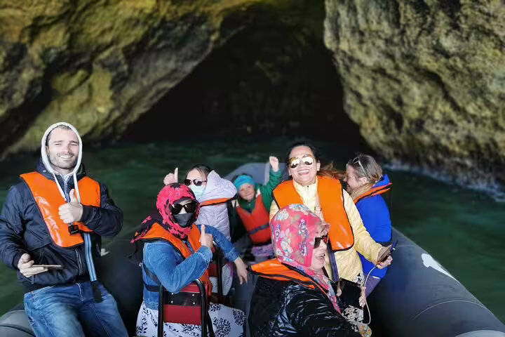 Tourists enjoy a boat trip through the Benagil Caves during a private Algarve tour from Lisbon, wearing life vests and smiling.