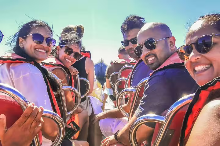 Group enjoying a sunny boat tour to Benagil Caves during Algarve full-day private trip from Lisbon, wearing life jackets and sunglasses.